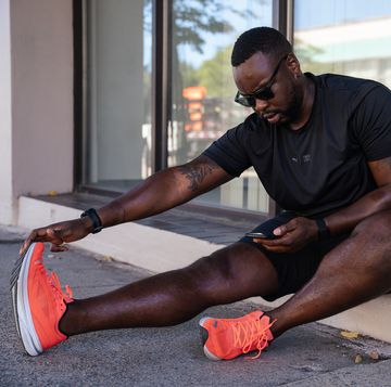 man stretching his hamstring after a run while looking at his phone