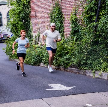 two runners run past a brick building covered in ivy