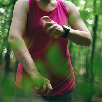 woman athlete using mosquito repellent in a forest